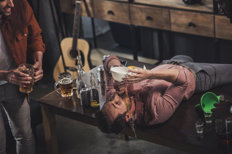 Young Man Lying on Table and Drinking Beer from Funnel while Friends