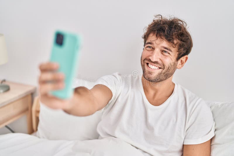 Young Man Make Selfie by Smartphone Sitting on Bed at Bedroom Stock