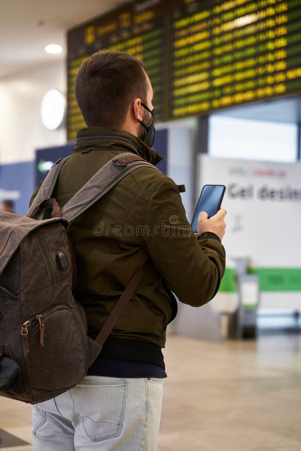Young Man with Mask at the Airport Looking at Flight Schedule through