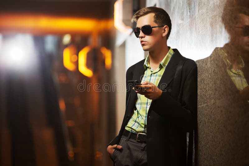 Young fashion man with mobile phone at the wall