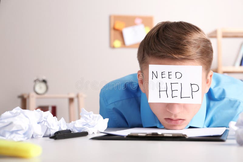 Young man with note NEED HELP on forehead at workplace