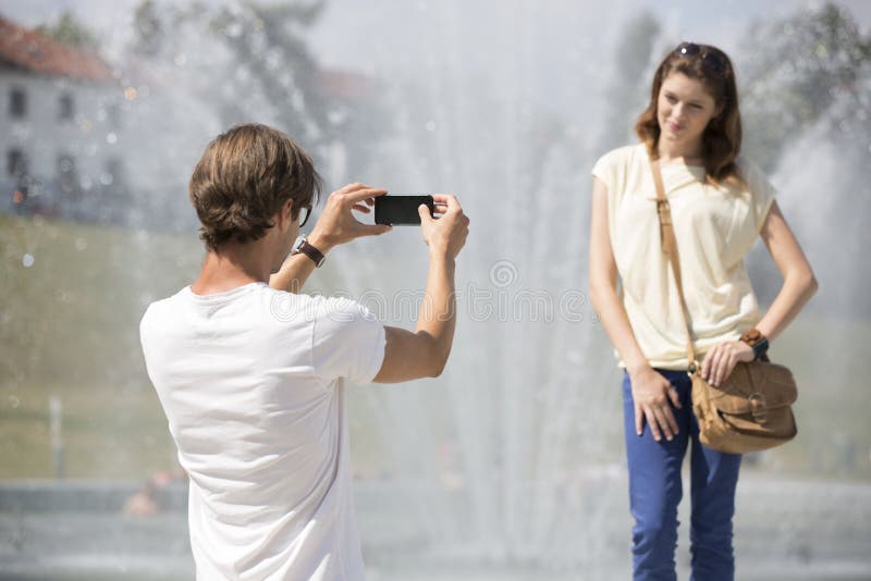 Mladý muž fotografovanie žena proti fontány.
