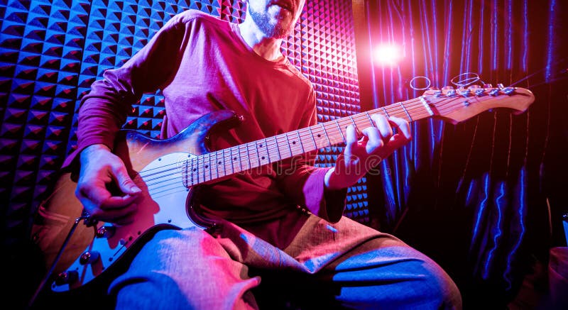 Young man playing on the guitar in sound recording studio. royalty free stock photos