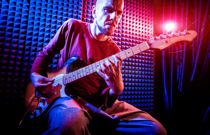 Young man playing on the guitar in sound recording studio. stock photo