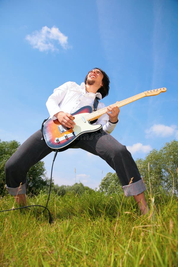 Young man plays on guitar on grass