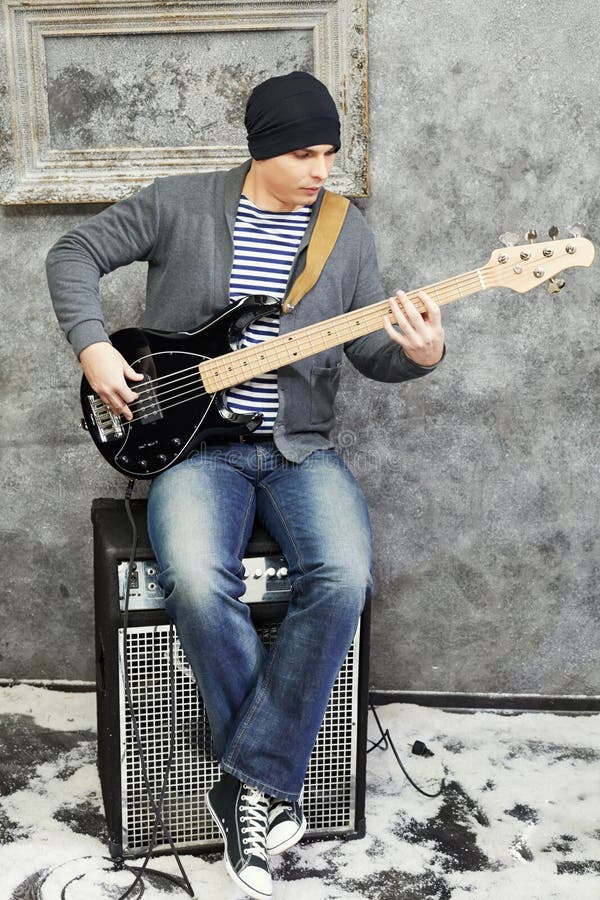 Young man plays guitar sitting on amplifier