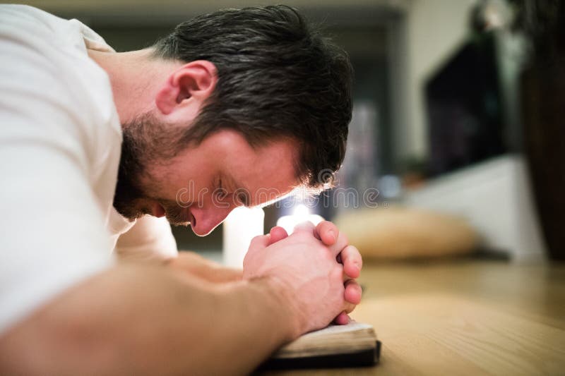 Young man praying, kneeling on the floor, hands on Bible royalty free stock image Young man praying, kneeling on the floor, hands on Bible royalty free stock image