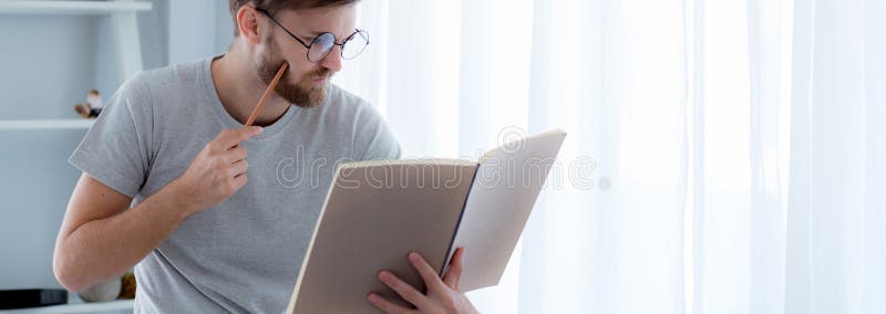 Young man reading book preparing exam at room, male learning and homework