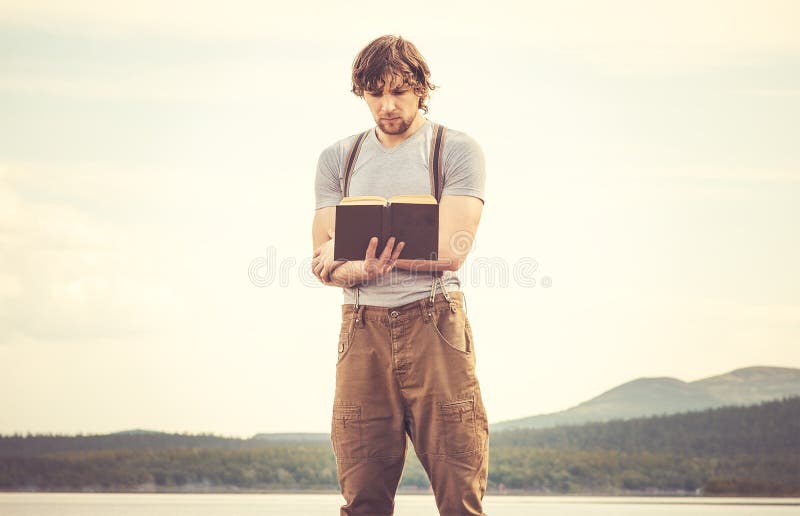 Young Man reading book standing outdoor. With mountains on background Summer vacations and Lifestyle concept royalty free stock image Young Man reading book standing outdoor. With mountains on background Summer vacations and Lifestyle concept royalty free stock image
