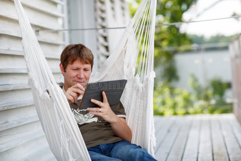 Young man relaxing in hammock and using tablet computer