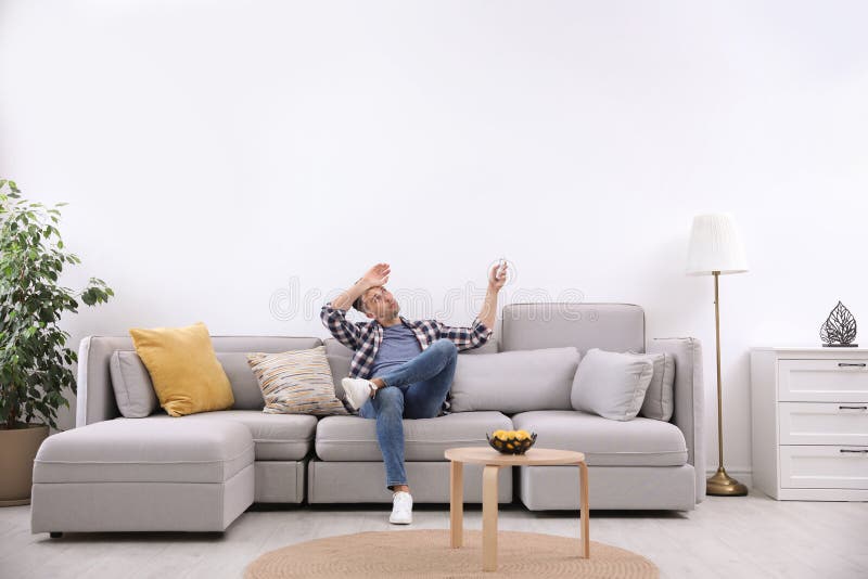 Young Man with Remote Control Suffering from Heat Under Broken Air