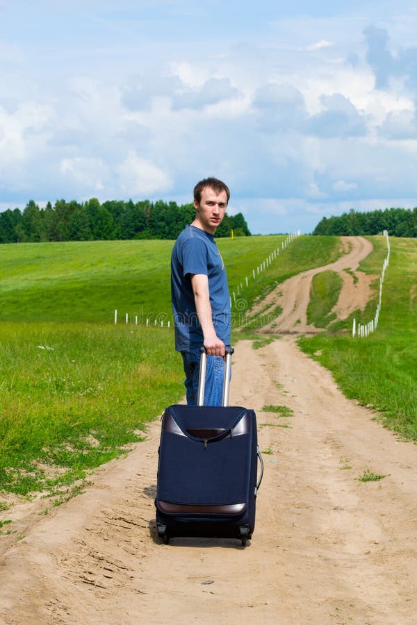 The young man on road in field with a suitcase
