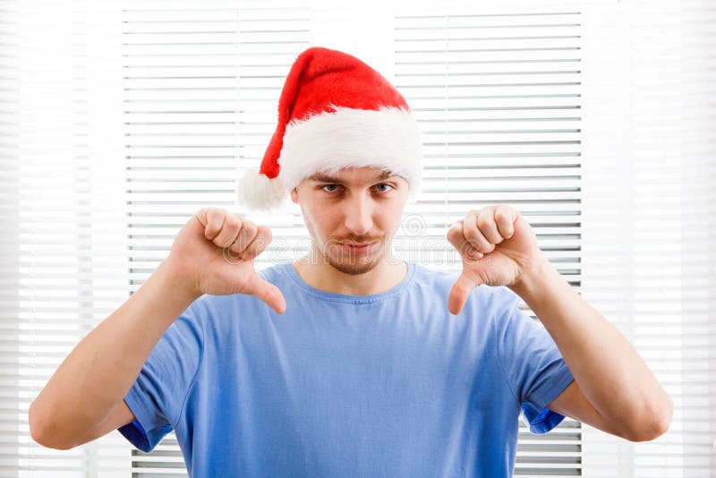 Young Man in Santa Hat make Thumb Down on the Jalousie Background