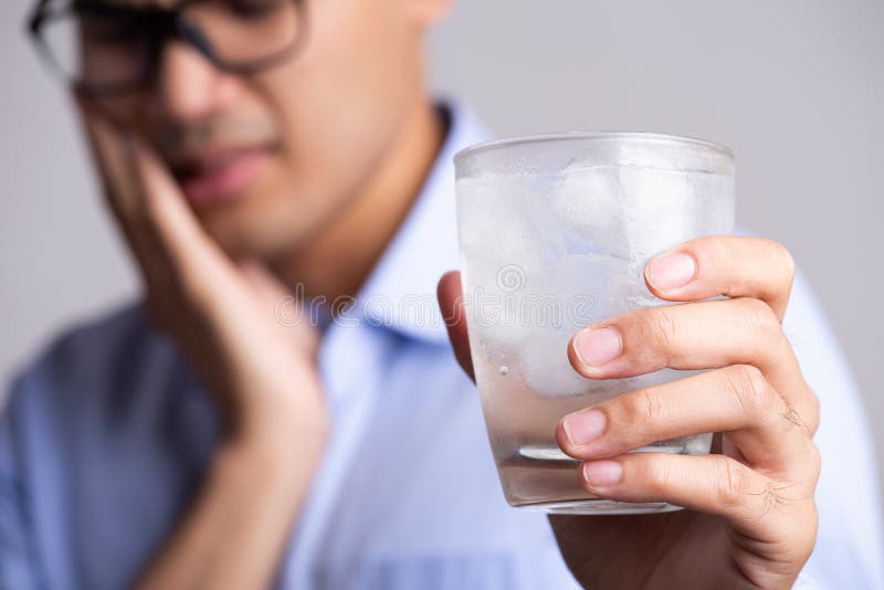 Young man with sensitive teeth and hand holding glass of cold water with ice. Healthcare concept