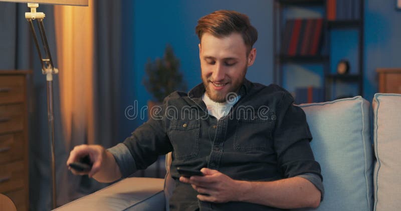 A young man sits contentedly on the couch in the living room in the evening