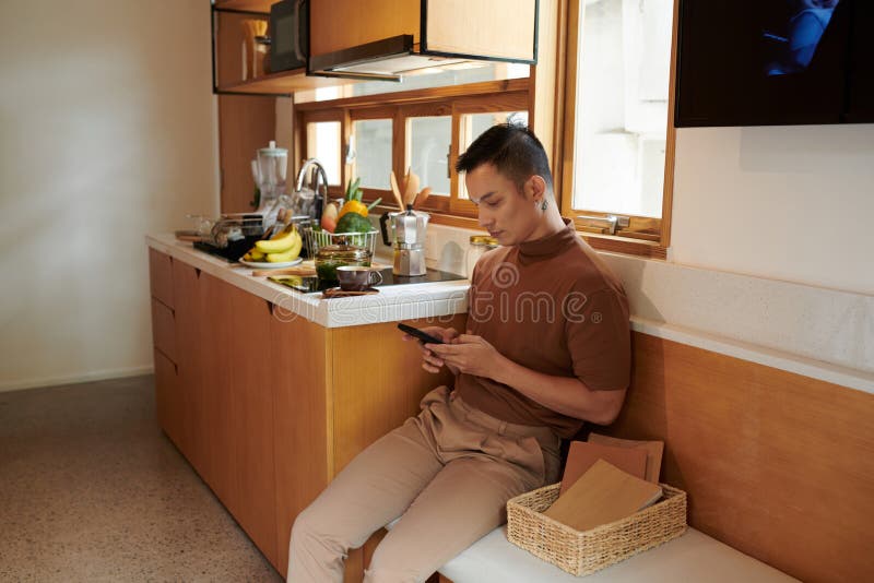 https://thumbs.dreamstime.com/b/young-man-sitting-bench-kitchen-testing-friends-smartphone-asian-young-man-texting-250325780.jpg