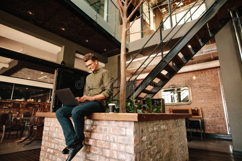 Young man sitting in office cafeteria working on laptop. Creative executive using laptop computer during coffee break.