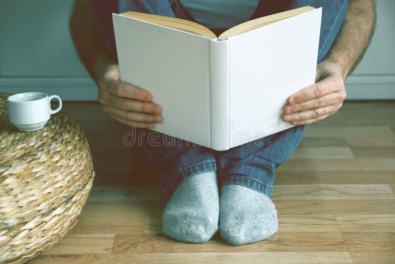 Young man sitting on the wooden floor drinking coffee while reading a book. Empty copy space royalty free stock photo