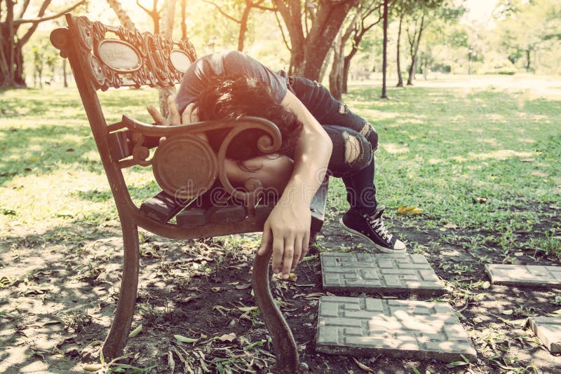 Young man sleeping on bench outdoor in city park during day