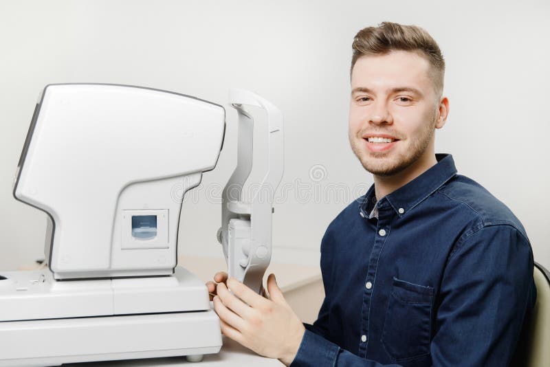 Young man smiles reception doctor ophthalmologist to check eyes of patient on device with laser.