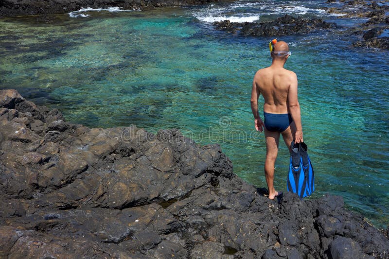 Young man with snorkeling equipment on the rock coast