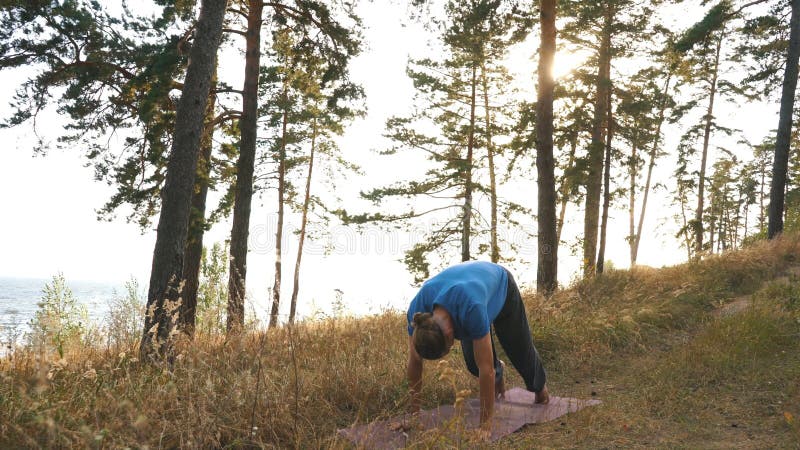 Young man standing in the Downward Facing Dog position in the wood under river
