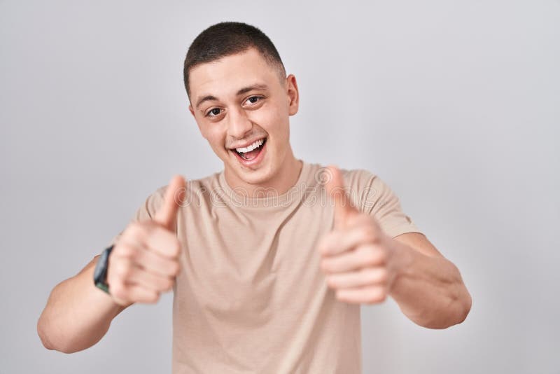 Young man standing over isolated background approving doing positive gesture with hand, thumbs up smiling and happy for success