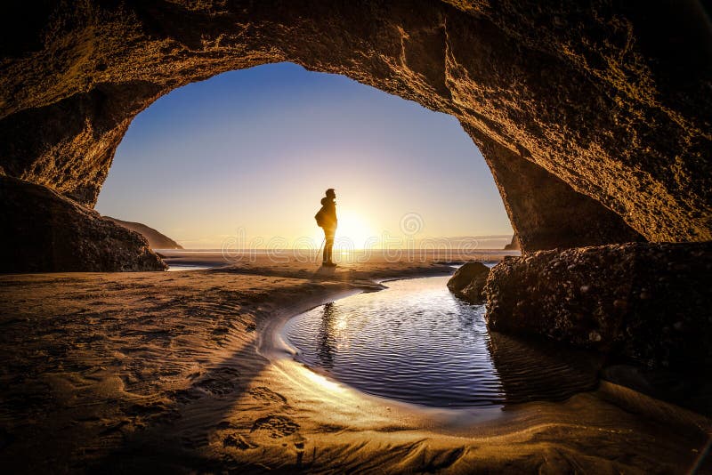 Young man stands at a cave exit. A person deep thinking at the exit of a cave. Beautiful landscape formation of a cave in New Zealand. Young man stands at a cave exit. A person deep thinking at the exit of a cave. Beautiful landscape formation of a cave in New Zealand