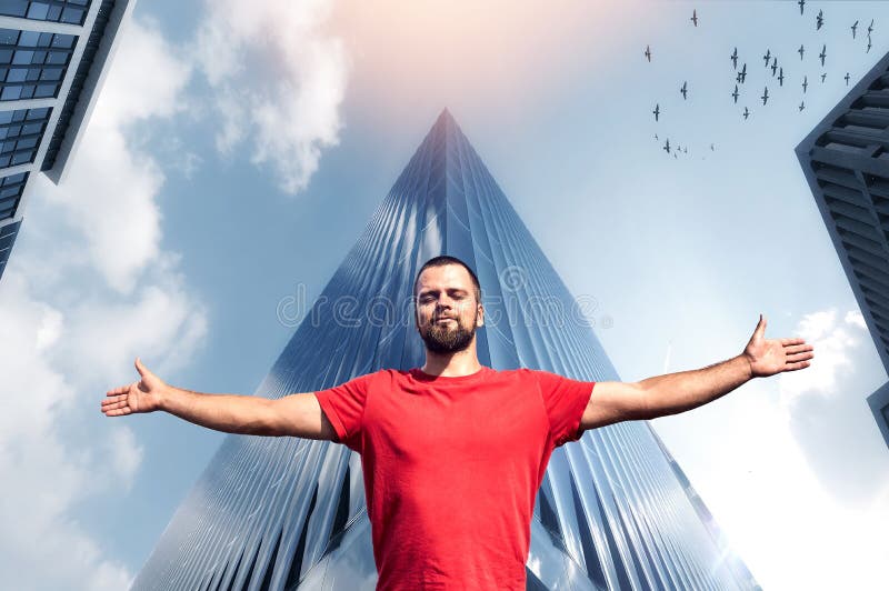 Portrait of free and happy man with both arms wide open facing the bright sunshine against blue sky and modern buildings in the background. Portrait of free and happy man with both arms wide open facing the bright sunshine against blue sky and modern buildings in the background