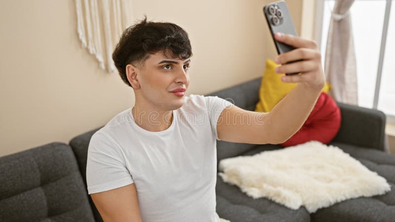 A young man takes a selfie in a modern apartment living room, showcasing a casual, connected lifestyle stock photos