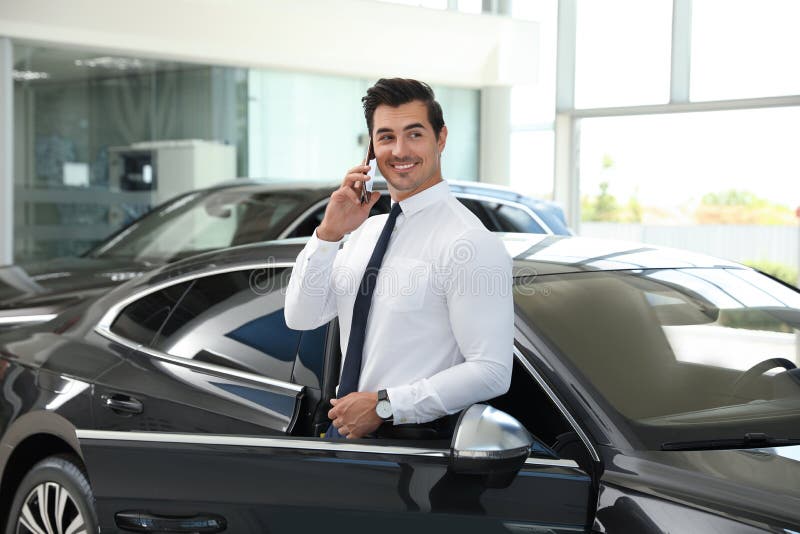 Young man talking on phone near car in dealership