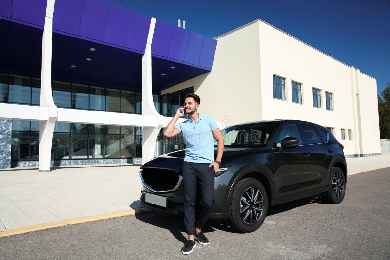 Young man talking on phone near modern car