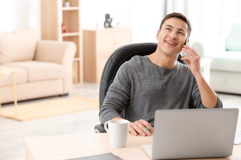 Young man talking on phone while working with laptop in home office