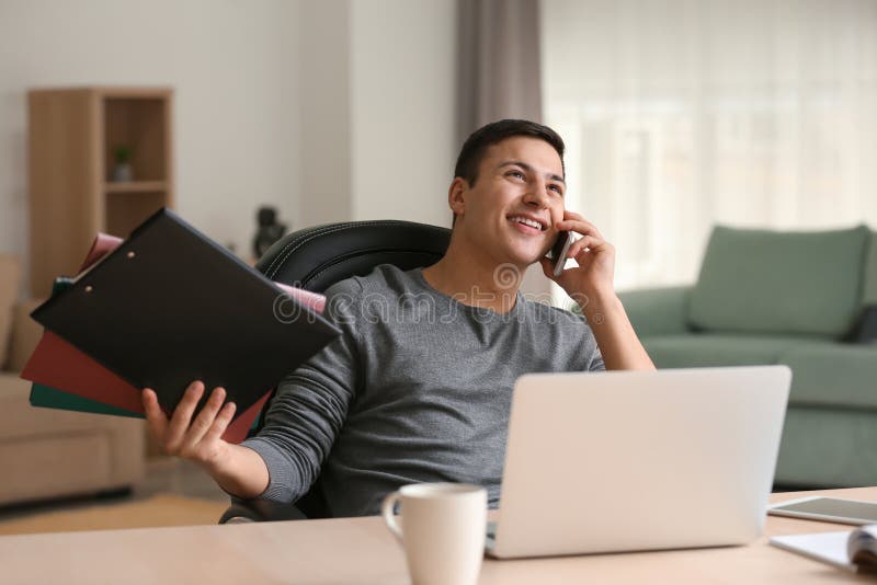 Young man talking on phone while working with laptop in home office