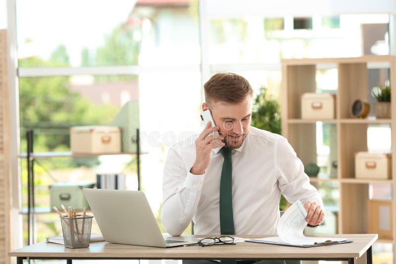 Young man talking on phone while working with laptop