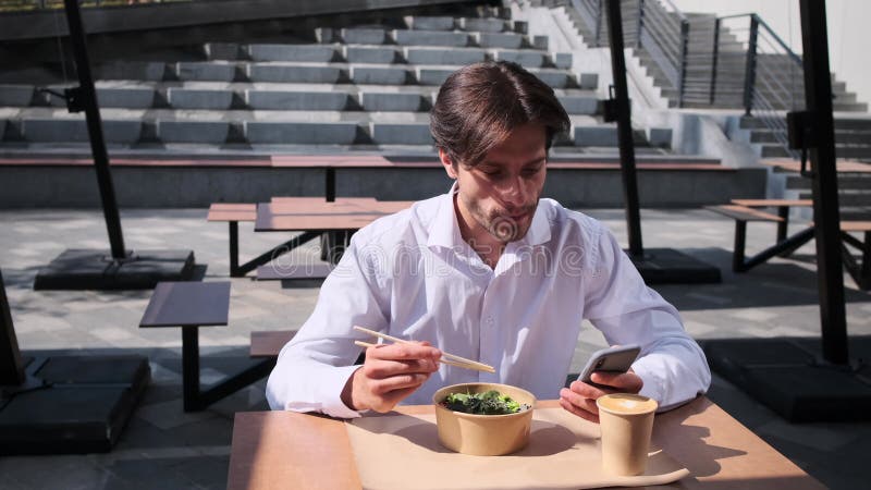 Young man text messaging using mobile phone while having lunch stock video