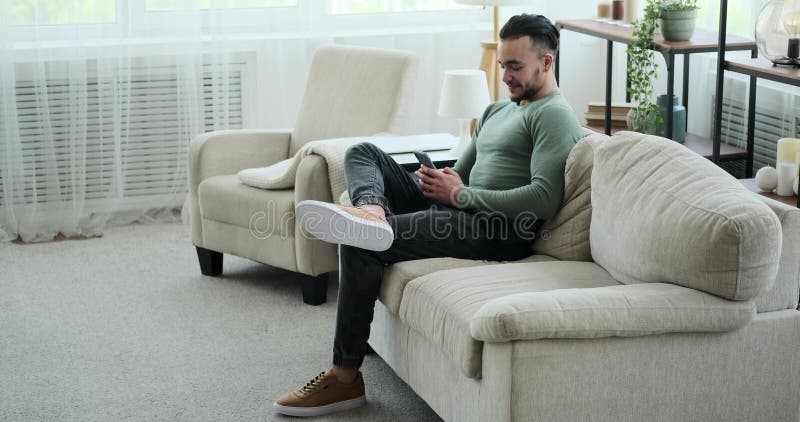 Young man text messaging using mobile phone while sitting on sofa stock video