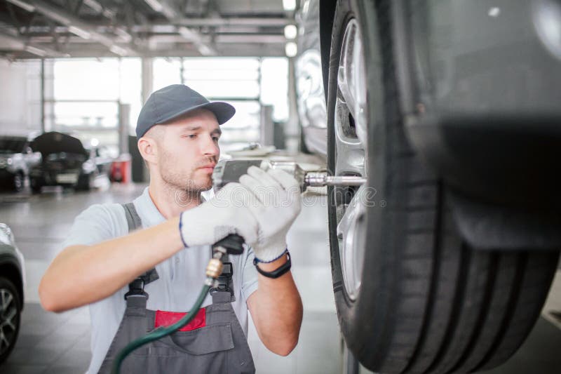 Young man in uniform stand at car which is on platform an repair wheel. He uses special wrenches for that. Worker is royalty free stock photos Young man in uniform stand at car which is on platform an repair wheel. He uses special wrenches for that. Worker is royalty free stock photos