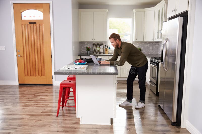 Young Man Using Laptop In Apartment Kitchen