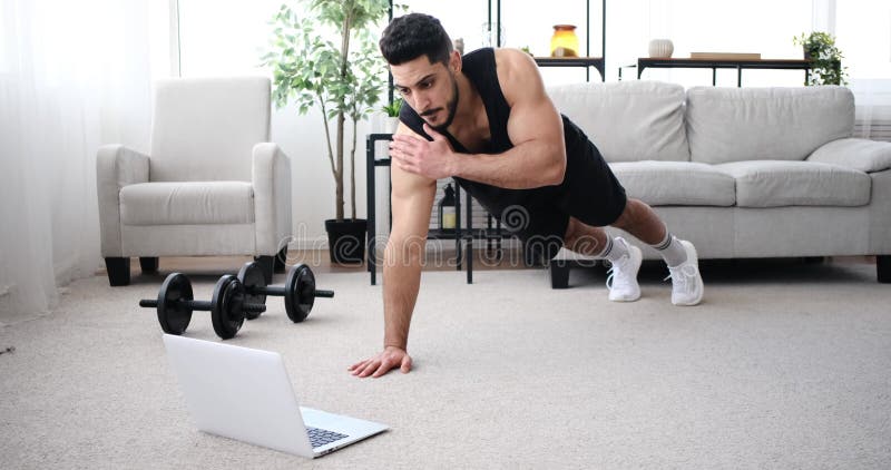 Young man using laptop while doing plank shoulder tap exercise stock video