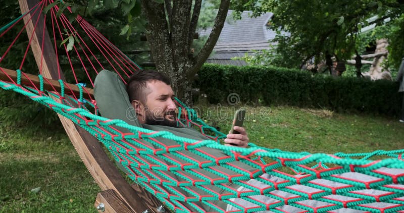 Young man using mobile phone while lying on hammock