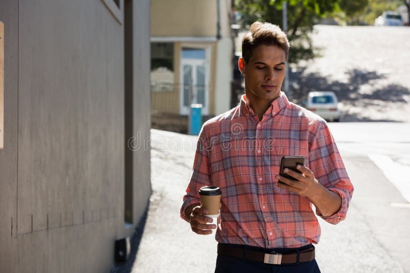 Young man using phone while walking by building in city