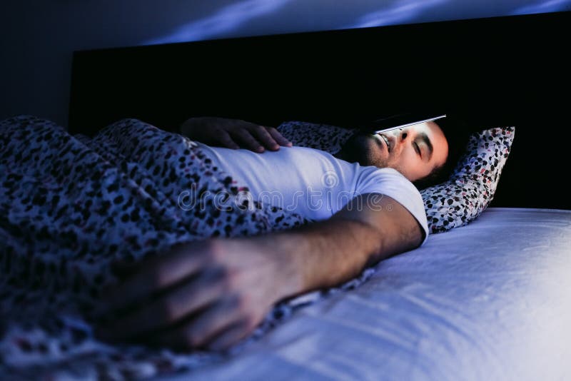 Young Man Using Smartphone In Bed At Night Stock Photo