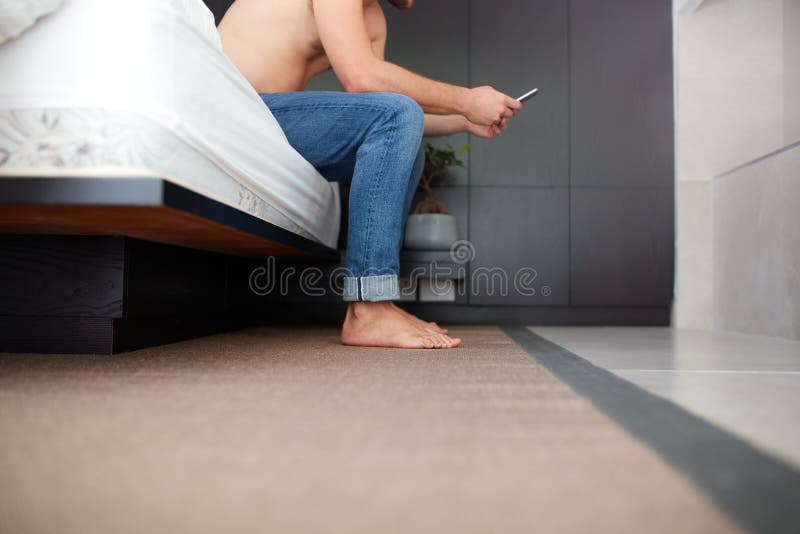 Young man using a tablet on the edge of his bed.
