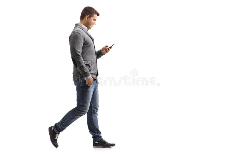 Full length profile shot of a young man walking and using a phone isolated on white background