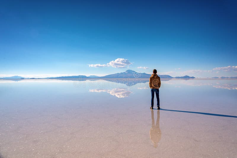 Young man watching the scenery and miror effect in Salar de Uyuni Uyuni salt flats, Potosi, Bolivia South America