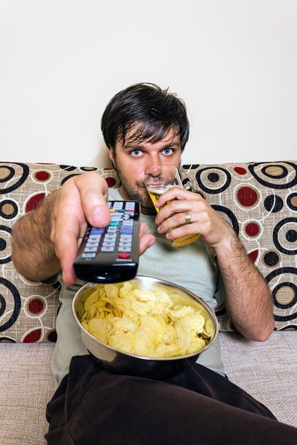 Young Man Watching Television, Eating Potato Chips and Drinking Stock