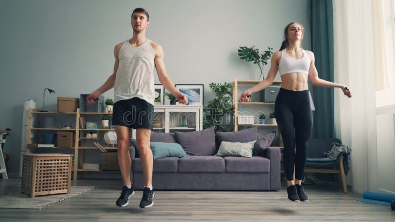 Young man and woman couple jumping rope in house together doing sports indoors