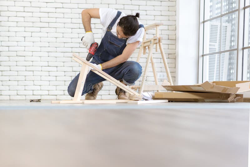 Young man working as handyman, assembling wood table with equipments, concept for home diy and self service.in the office there is a white brick block.