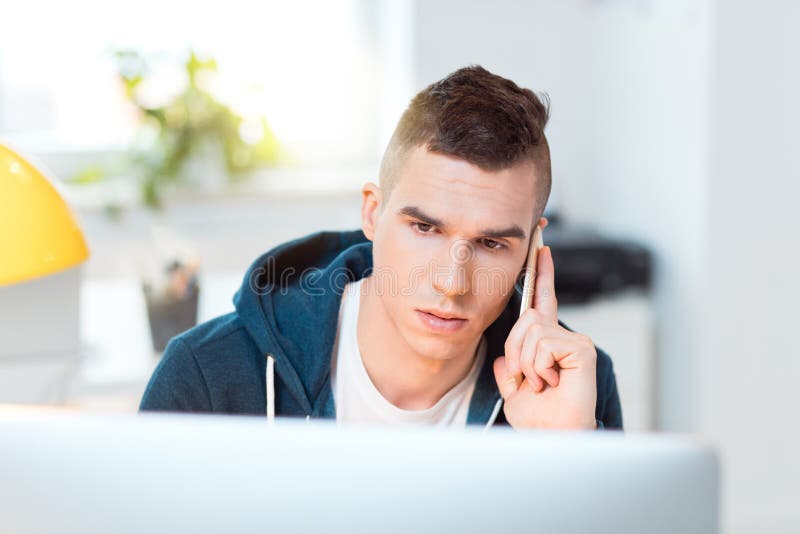 Young man sitting by computer and using mobile phone royalty free stock photo Young man sitting by computer and using mobile phone royalty free stock photo